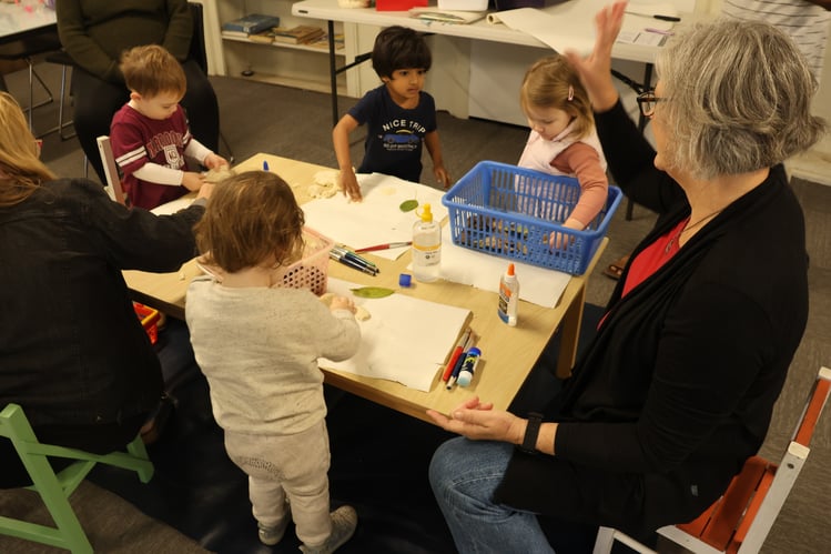 Sarah sits and does playdough and craft using found leaves with the children at playgroup.