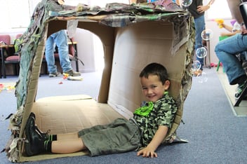 A young boy sits inside a cardboard box creation as part of creative and dramatic play