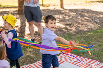 Child playing with rainbow ribbons engaged in physical play at playgroup in the park