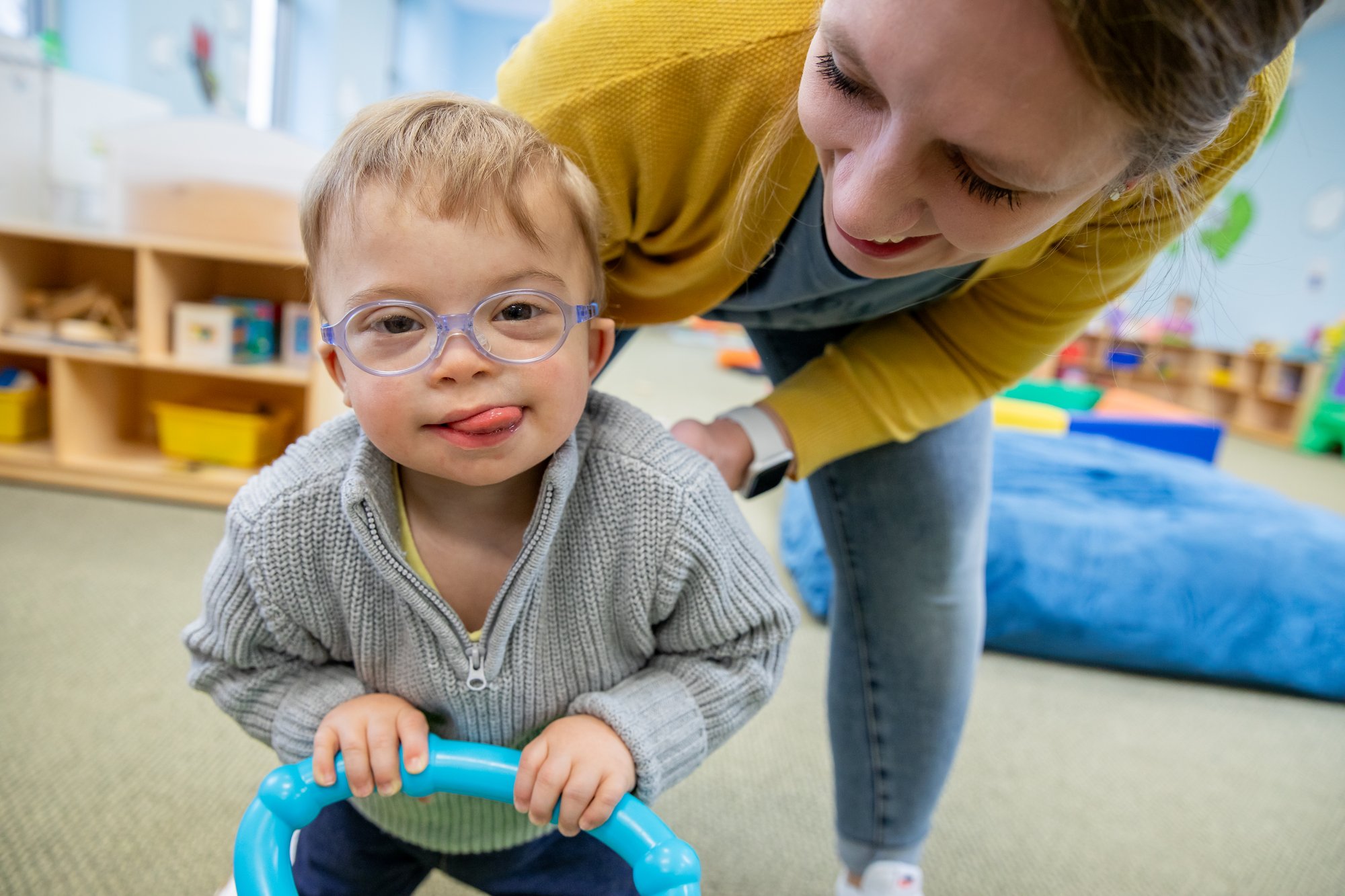 A mother plays with her child a a small assistive walker.