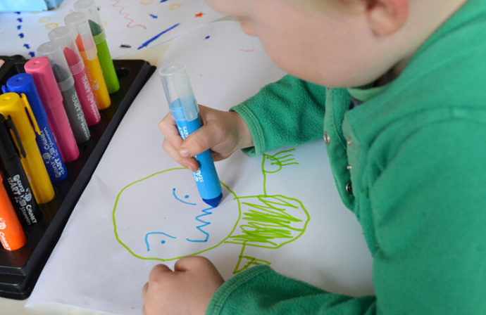 A young child draws emotions with big markers.